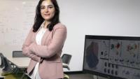 Elham Azizi standing arms crossed in front of a computer with data visualizations