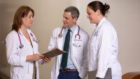 Three doctors standing and looking at a chart