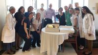 Large group of doctors, nurses, and patients stand next to a cake