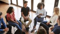 Young women and men gathered in a circle in discussion.