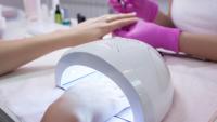 Photo of a person getting a manicure and drying nails under UV nail polish dryer.