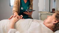 A patient laying down while their doctor holds their hand.