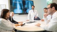 Brian Henick standing at the head of a table with other HICCC researchers sitting around and discussing. There is imaging of a chest cavity on a screen behind Henick.