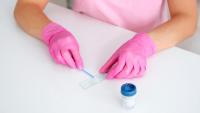 A person in pink scrubs and gloves swiping a swab across a microscope slide.