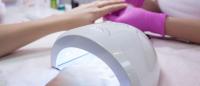 Photo of a person getting a manicure and drying nails under UV nail polish dryer.