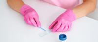 A person in pink scrubs and gloves swiping a swab across a microscope slide.